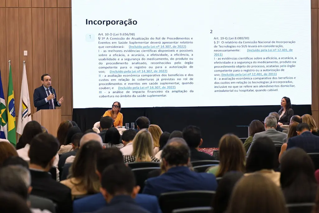 Foto horizontal que mostra um auditório lotado de pessoas assistindo a palestra do juiz Gerardo Humberto. No palco, há um enorme telão com a apresentação da palestra.